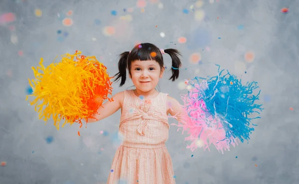 Little girl child cheerfully throws up colorful tinsel and confetti on a gray blue background. — Stock Photo, Image