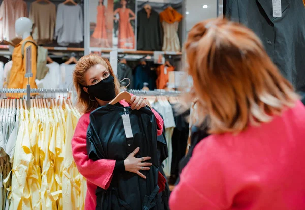 beautiful woman with phone bright pink shopping Mall coat with black protective mask on her face from virus infected air. concept of virus protection in the fashion, beauty, and shopping industries.