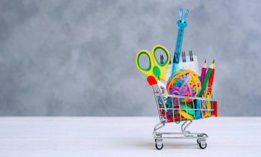 Gri bir arka planda alışveriş arabasında çok renkli okul gereçleri ve metin için kopya alanı.