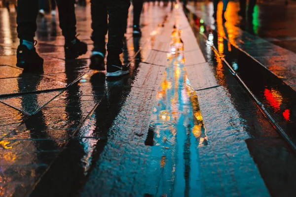 Rainy night in a big city, reflections of lights on the wet road surface. The view from the street level. Pedestrian feet and abstract background.