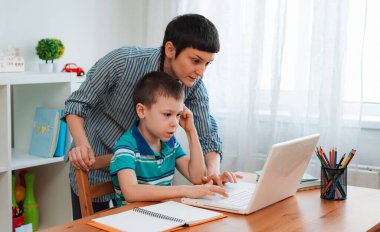 Anne ve çocuk okulu öğrencisi evde dizüstü bilgisayarla ödev öğreniyor. Salgın ve koronavirüs döneminde evde eğitim görmüş. Ebeveyn yardımı eğitimi.