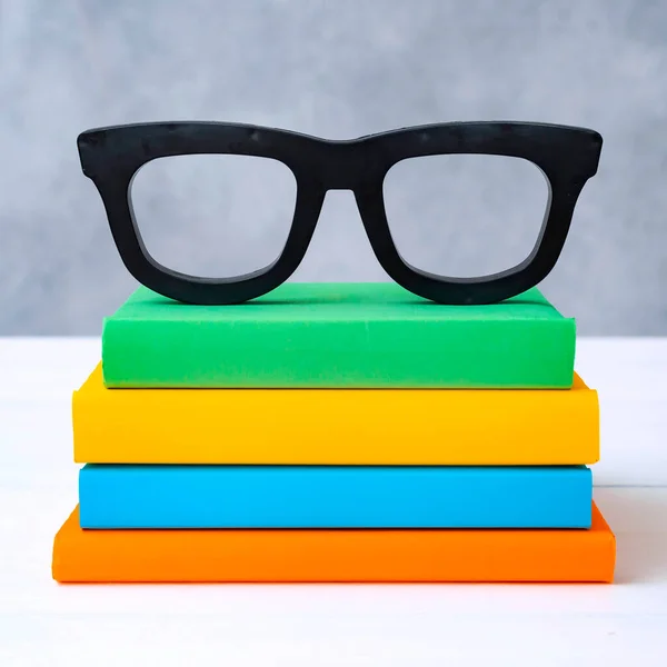 stack of colorful books with glasses on a white wooden table against a gray wall. The concept of going back to school, reading, library, literature, study, education.