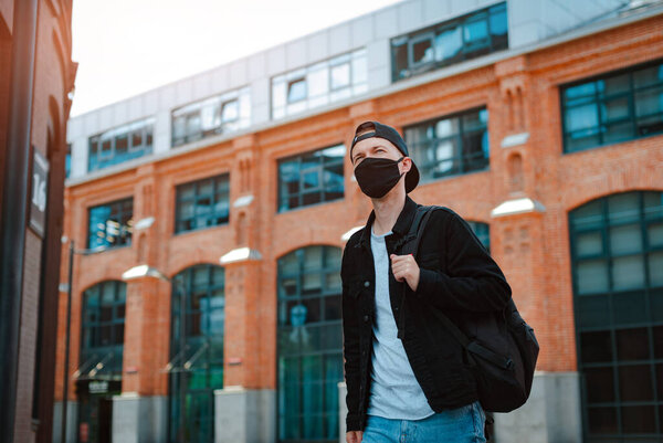 Portrait of a modern guy in a surgical black mask against the background of a modern megalopolis building, coronavirus, disease, infection, quarantine, medical mask, new normal, pandemic
