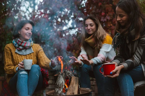 Tres amigos relajarse cómodamente y beber vino en una noche de otoño al aire libre por el fuego en el patio trasero. — Foto de Stock