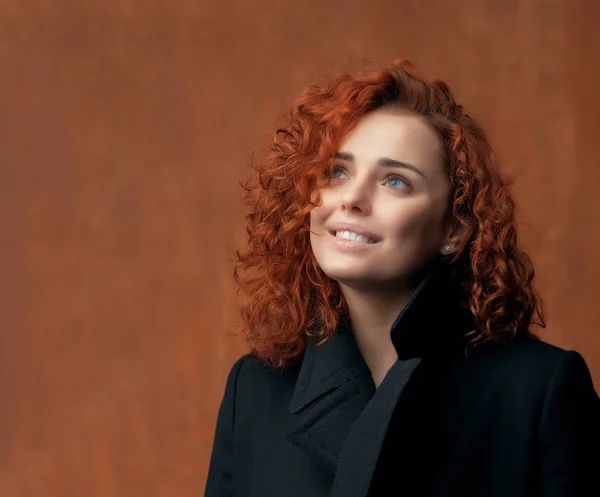 young redhead woman posing at studio, smiling and looking up