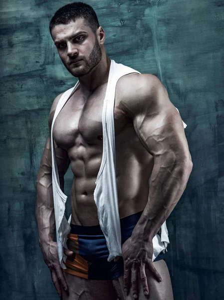 Muscular bodybuilder wearing ripped shirt posing at studio