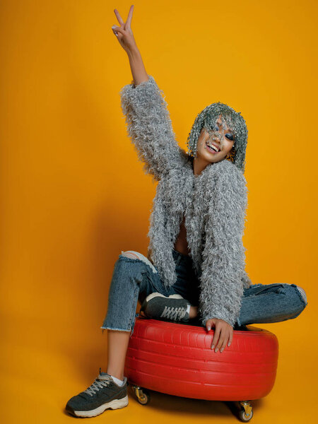 model with pin wig wearing stylish clothes posing on yellow background