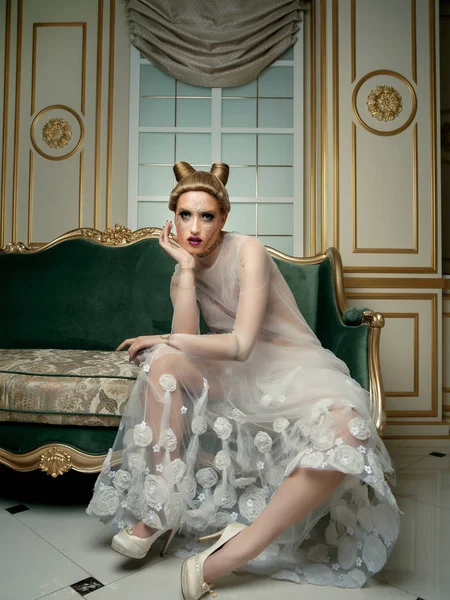 模型与创造性的化妆在透明的礼服摆在沙发上 — 图库照片