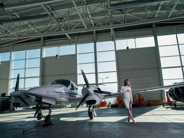 Beyaz elbiseli genç kadın uçağın yanında poz veriyor.