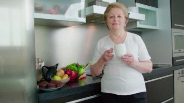 Son sınıf öğrencisi kadın mutfakta fincandan içiyor.