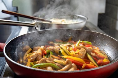 Hob üzerinde kırmızı tavada tavuk ve sebze kızarmış