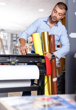 male printing worker with rolls of colored paper clipart