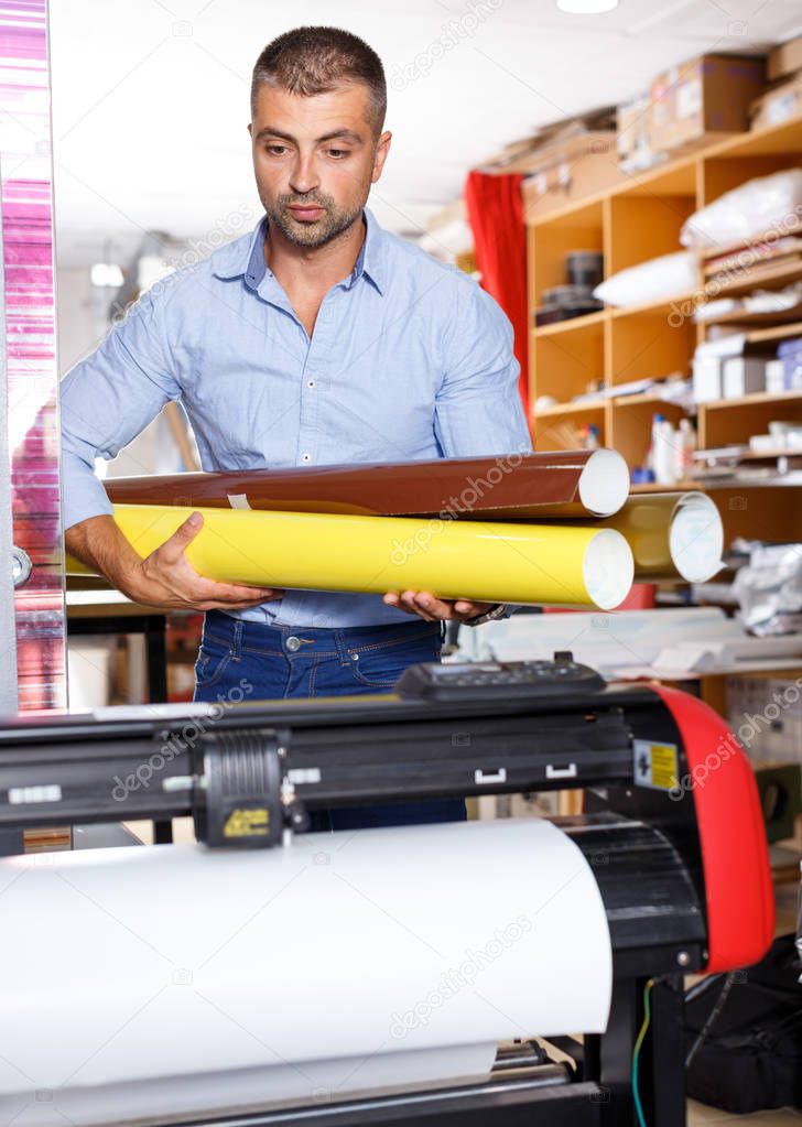 male printing worker with rolls of colored paper