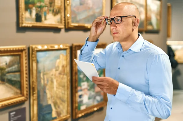 Portrait of man with a guide looking at pictures at museum