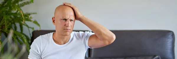 Feeling depressed. Desperate young man keeping his hand on forehead while sitting on the couch at home — Stock Photo, Image