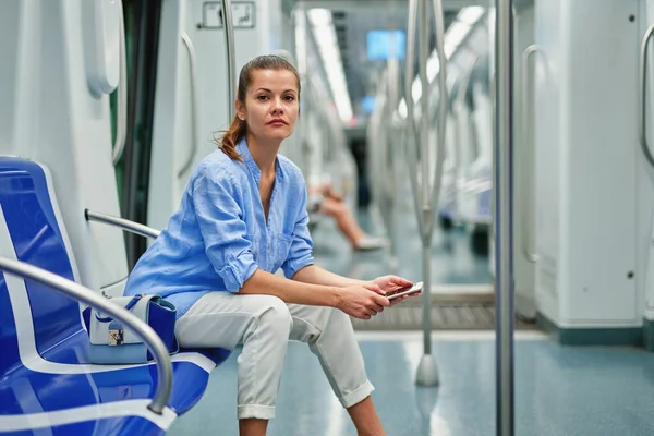 Positief brunette meisje met behulp van mobiele telefoon in de metro. — Stockfoto