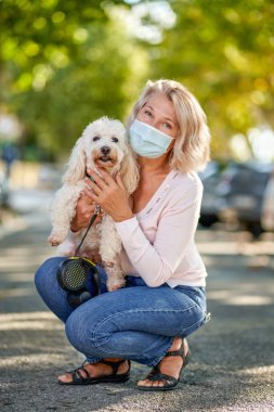 Olgun bir kadın köpeğiyle dışarıda geziyor antivirüs maskesi.
