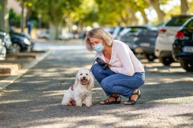 Olgun bir kadın köpeğiyle dışarıda geziyor antivirüs maskesi.