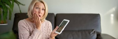 Kanepede oturup dijital tablet kullanan olgun bir kadın. Evdeki tablet üzerinden internet taraması.