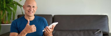 Adam kanepede oturuyor ve dijital tablet kullanıyor. Evdeki tablet üzerinden internet taraması.