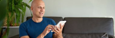 Adam kanepede oturuyor ve dijital tablet kullanıyor. Evdeki tablet üzerinden internet taraması.