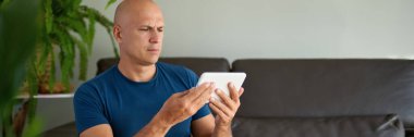 Adam kanepede oturuyor ve dijital tablet kullanıyor. Evdeki tablet üzerinden internet taraması.