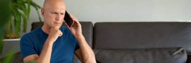 Evde akıllı telefon kullanan bir adam evdeki koltukta oturuyor.