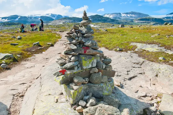 Dağlarla, turistlerle dolu güzel bir manzara ve Norveç 'in Finse kentindeki Hardangerjokulen buzulunda yer alan Mavi Buz (Blaisen) buz sahasına giden yolda taş cairn ve kırmızı T harfleriyle işaretlenmiş bir yol.