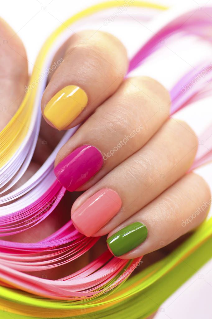 Multi-colored manicure with pink,green, yellow and peach nail Polish close-up.Summer bright manicure on short nails.