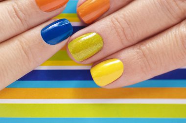 Çizgili arka plan yakın çekim turuncu, mavi, sarı oje ile renkli parlak manikür. Tırnak sanat.