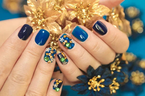 Bright blue manicure with the design of rhinestones of different shapes and colors on the nails close up. Nail art.