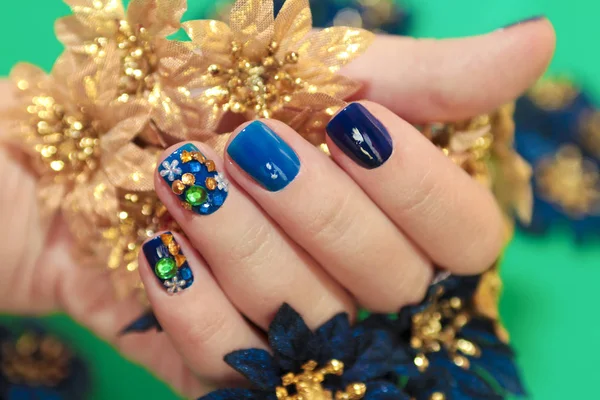 Bright blue manicure with the design of rhinestones of different shapes and colors on the nails close up. Nail art.