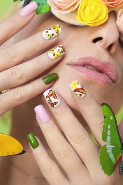 Multi-colored manicure on nails with a design of butterflies. Decorated glasses with flowers and butterflies on a girl with light lipstick. Nail art.