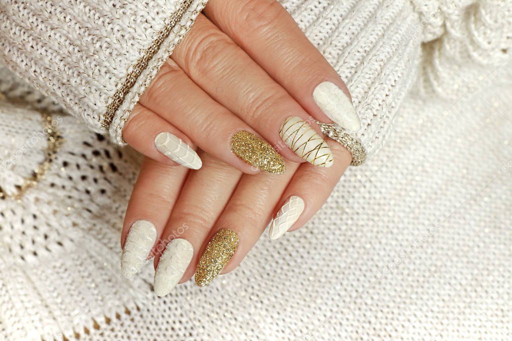 Knitted sand manicure on long oval nails with golden sequins and threads on a woman's hand in a jacket. Winter trend in nail design.