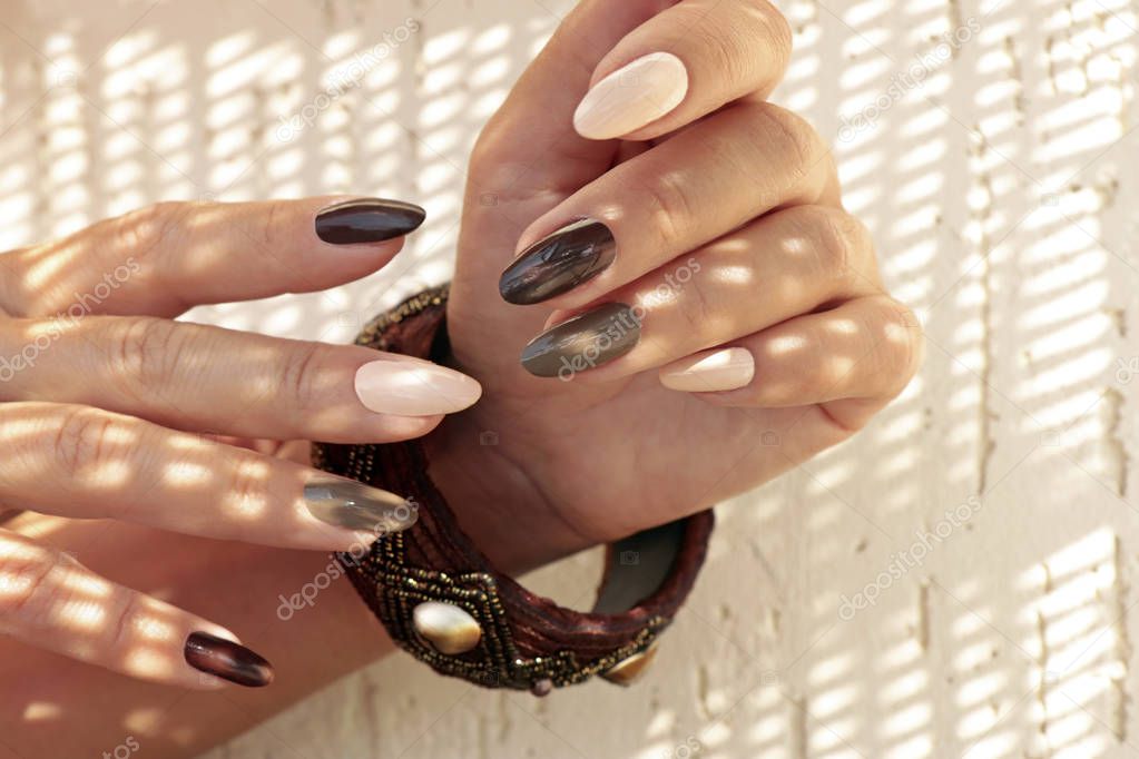 Multicolored brown milk manicure on oval long nails and a bracelet on his hand in the sun glare in the summer.