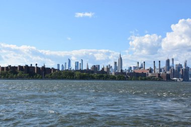 New York City - Haz 30: Manhattan Manzarası, New York, Brooklyn'deki Domino Park'tan, 30 Haziran 2019'da görüldüğü gibi. New York, ABD'nin nüfusa göre en büyük şehridir ve yıllık milyonlarca ziyaretçisi vardır..