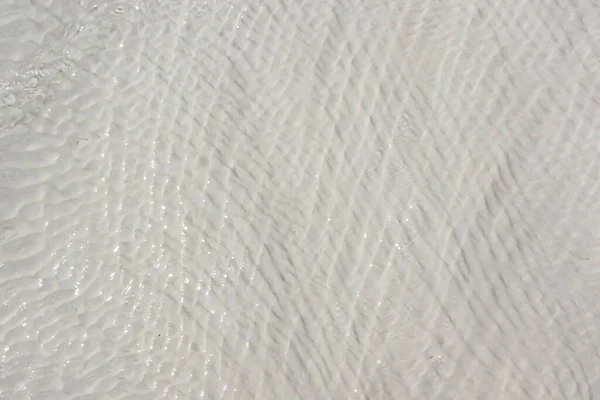 Beyaz travertin yüzeyinin arkaplanı dalgalarla kaplı berrak suyla kaplı.