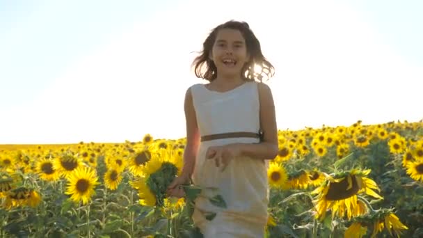 Malé radostné holčičky běží šťastný zdarma přes pole s slunečnice. zpomalené video. vonící velké slunečnice na letní pole. Radost z příjemného života vůně. Letní dovolená. koncepce