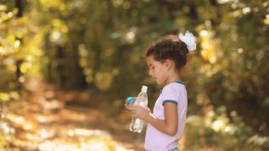 küçük kız sonbahar ormanın içinde plastik bir şişe su içer. Sonbahar güzel ormandaki küçük kız susadı. küçük kız sonbahar kavramı yaşam tarzı