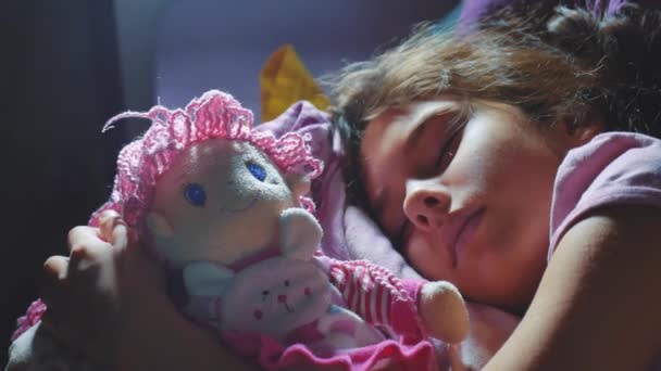 Aranyos kislány a rekamié aludni, és ölelés neki baby doll. barna kislány alszik éjszaka az ágy életmód gyermekkori szerelmét. gyermekek alvás koncepció — Stock videók