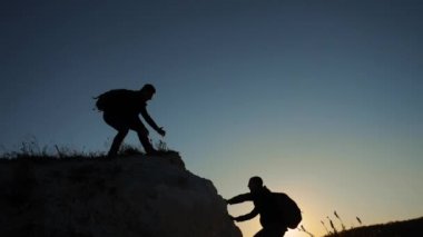 siluet iki erkek takım çalışması turist tırmanıcı bir dağa tırmanıyor. yürüyen turist macera dağcılar günbatımı Tırmanma dağ hiking. ağır çekim video. Uzun yürüyüşe çıkan kimse güneş ışığı üstünde tepe tepe zafer kazanmak