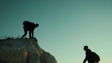siluet iki erkek takım çalışması turist tırmanıcı bir dağa tırmanıyor. yürüyen turist macera dağcılar günbatımı Tırmanma dağ hiking. ağır çekim video. Uzun yürüyüşe çıkan kimse güneş ışığı üstünde tepe tepe zafer kazanmak