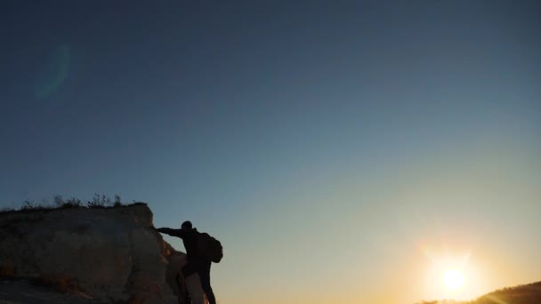 Σιλουέτα πεζοπόρος άνθρωπος τουρίστες ορειβάτης ανεβαίνει ένα βουνό. περιπατητή πεζοπορία περιπέτεια ορειβάτες ηλιοβασίλεμα ανάβαση στο βουνό. βίντεο αργής κίνησης. πεζοπόρος φως του ήλιου επάνω κερδίσει νίκη λόφο λευκό βράχο — Αρχείο Βίντεο