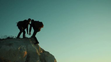 siluet iki erkek takım çalışması turist tırmanıcı bir dağa tırmanıyor. yürüyen turist macera dağcılar günbatımı Tırmanma dağ hiking. ağır çekim video. Uzun yürüyüşe çıkan kimse güneş ışığı üstünde tepe tepe zafer kazanmak