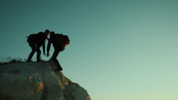 シルエット 2 つの男性は観光客チームワークの登山家は、山を登っていきます。歩いて観光ハイキングの冒険登山夕焼け登る山。スローモーション映像。上ハイカー日光勝利丘 — ストック動画