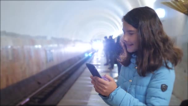 dívčí teenager v podzemní dráze metra v metru, čekající na příjezd vlaku, má telefon Smartphone. malá holčička bruneta, hledá Internet na webových stránkách životního stylu sociální sítě