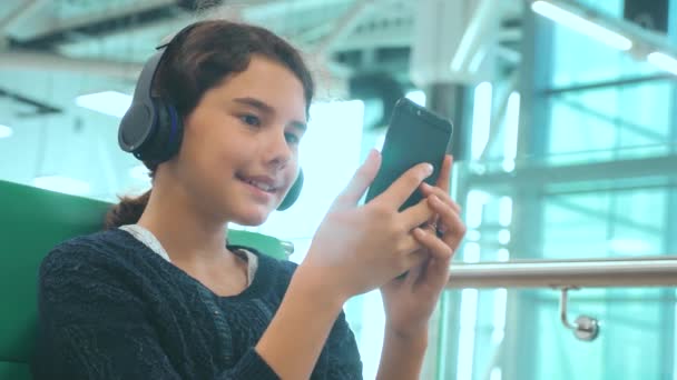 airport waiting hall room for a flight by plane. young happy teen girl in headphones lifestyle listening to the music on smartphone chatting communicates in the messenger. teenager girl in social
