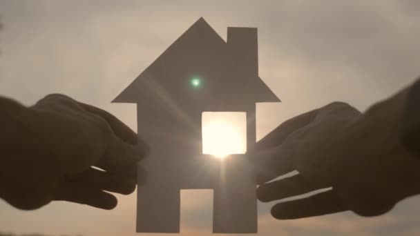 šťastný koncept výstavby rodinných domů. Muž, který drží doma papírový domek ve svých rukou při slunečním svitu ve stylu slunce. životní ekologie symbol videa