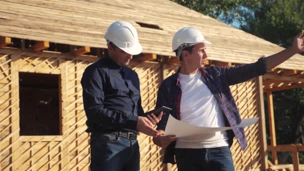 teamwork. concept building constructing architect slow motion video. two men builder in helmets study digital tablet the house plan. two architects working on construction of frame house business