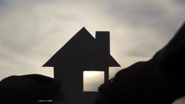 šťastný rodinný domek styl stavby. Muž, který drží doma papírový domek ve svých rukou při slunečním svitu siluetě. ekologie životní video symbol